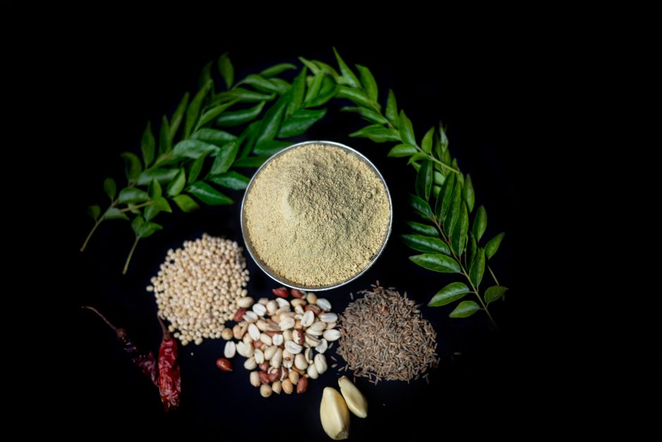 Flat lay of Indian spices and curry leaves on black. Includes cumin, garlic, peanuts, and more.