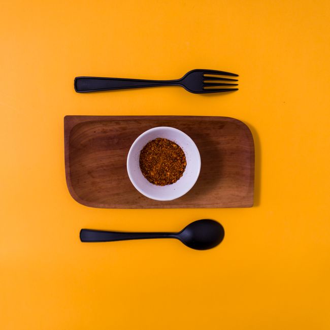 A minimalist flatlay featuring a spice bowl on wood with cutlery against a vibrant yellow background.
